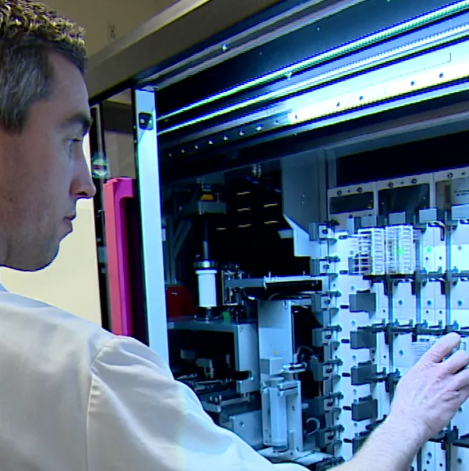 An Aiosyn colleague loading glass slides into the racks of a whole-slide scanner.